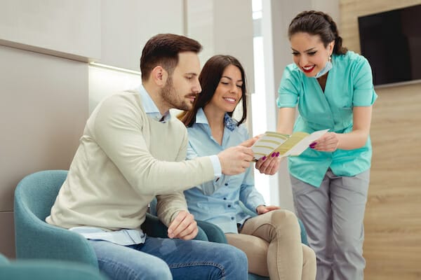 A couple sitting in a waiting room with a dental assistant going over an information brochure.
