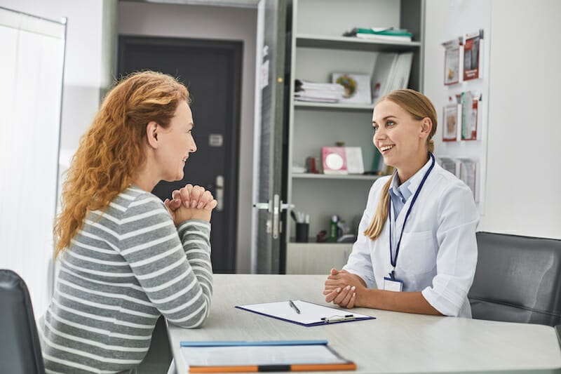 A female doctor talking to a female patient at a desk.